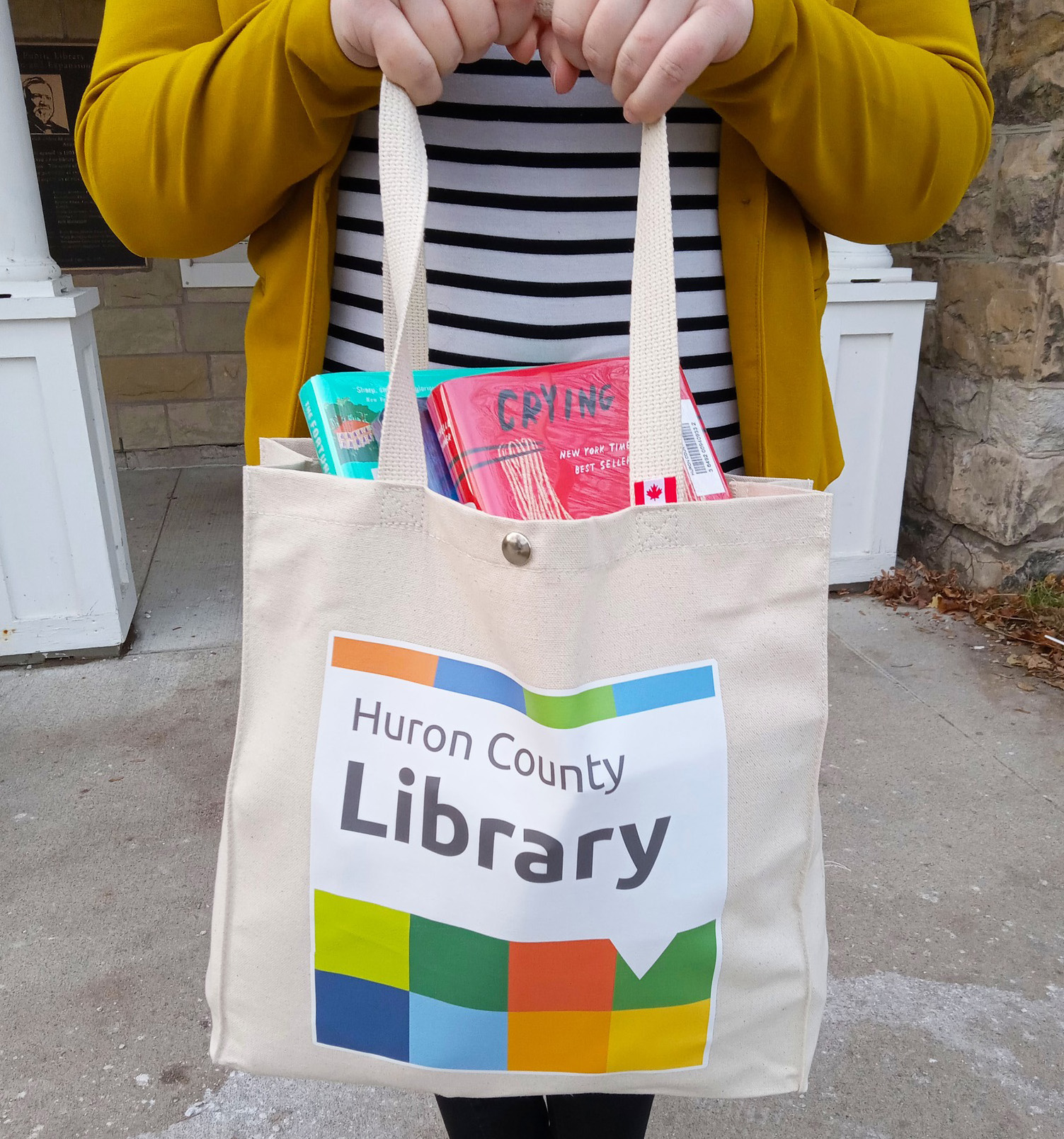 Image of a person holding up the new tote bags featuring the new Huron County Library logo on the front.